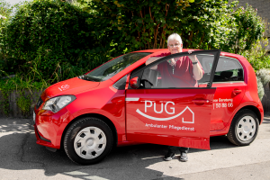 Pflegefachkraft steigt aus einem roten PuG-Pflegedienst-Auto für die ambulante Pflege.
